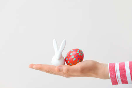 Female hand with figure of bunny and Easter egg on light backgroundの写真素材