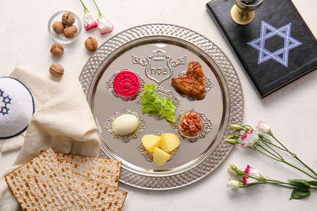 Passover Seder plate with traditional food, Torah and Jewish cap on white background