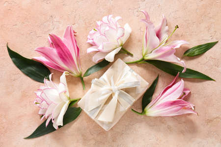 Beautiful lilies and gift on color backgroundの写真素材