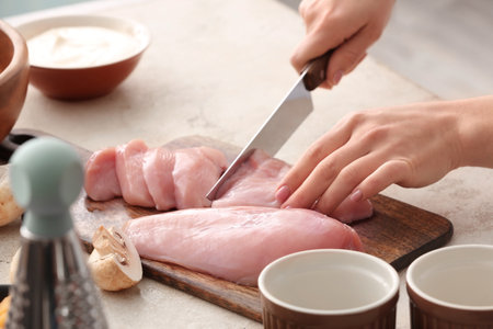 Woman cutting chicken fillet in kitchen, closeupの写真素材