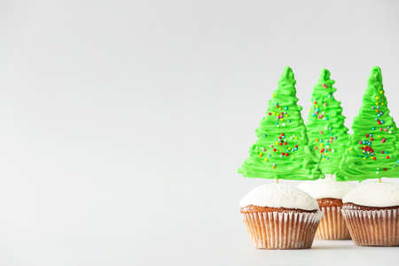 Tasty Christmas cupcakes on light background