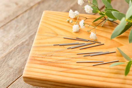 Stand with acupuncture needles and flowers on wooden backgroundの写真素材