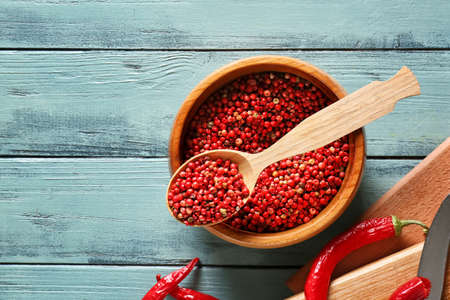 Bowl and spoon with red peppercorns on color wooden background