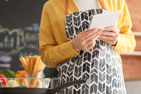 Young housewife with tablet computer cooking in kitchen at homeの写真素材