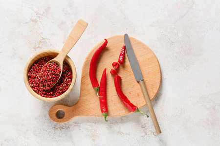 Bowl and spoon with red peppercorns and chili peppers on light backgroundの写真素材