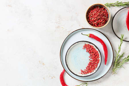 Bowl and plate with red peppercorns on light background
