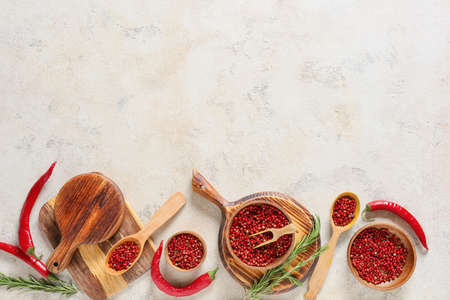 Bowls and spoon with red peppercorns on light background