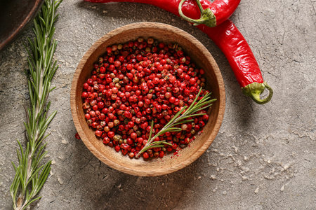 Bowl with red peppercorns on gray background