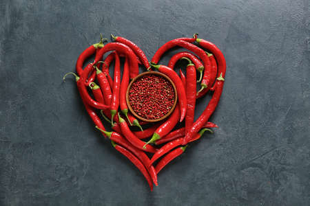Heart made of chili peppers and bowl with red peppercorns on dark backgroundの写真素材