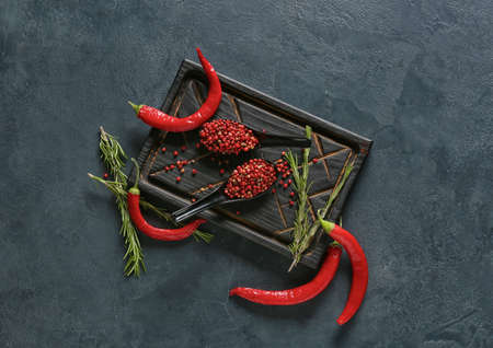 Spoons with red peppercorns and chili peppers on dark background