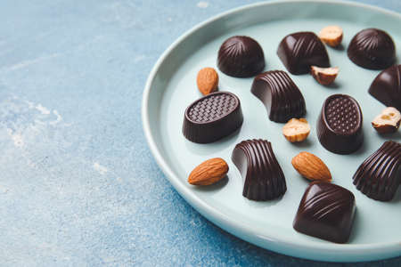 Plate with sweet chocolate candies and nuts on color background