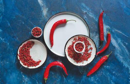 Plates and bowl with red peppercorns on color background