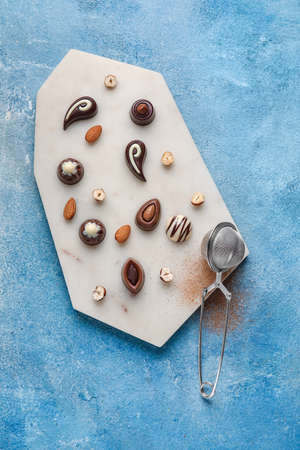 Board with sweet chocolate candies and nuts on color background