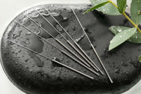 Acupuncture needles and spa stone on water, closeup