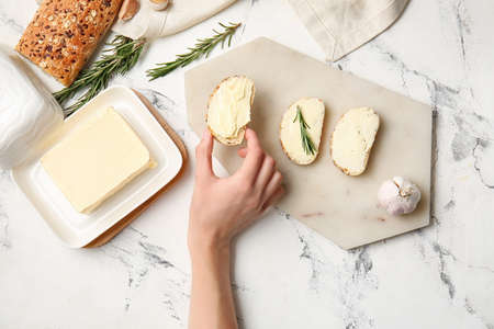 Woman holding slice of fresh bread with butter on light backgroundの写真素材