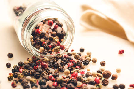 Overturned jar with mixed peppercorns on light background, closeup
