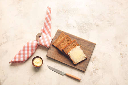 Board with slices of fresh bread and butter on light background
