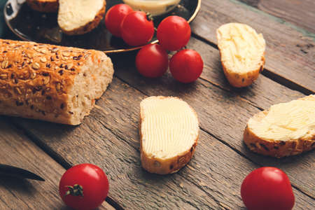 Slices of fresh bread with butter and tomatoes on wooden background
