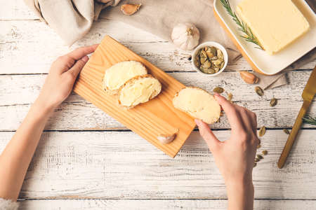 Woman holding slices of fresh bread with butter on light wooden background