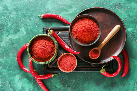 Bowls and spoon with red chili powder on color backgroundの写真素材