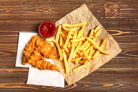 Tasty deep fried chicken wings with french fries and tomato sauce on wooden table