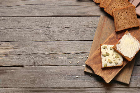 Slices of fresh bread with butter and pumpkin seeds on wooden background