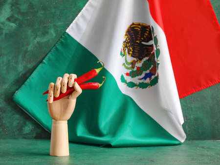 Wooden hand with chili peppers and Mexican flag on color background, closeup
