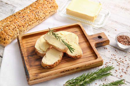 Slices of fresh bread with butter, flax seeds and rosemary on light wooden backgroundの写真素材