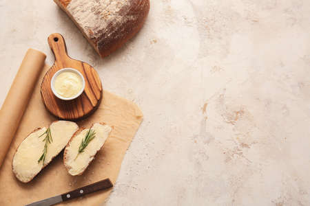 Slices of fresh bread with butter and rosemary on light backgroundの写真素材