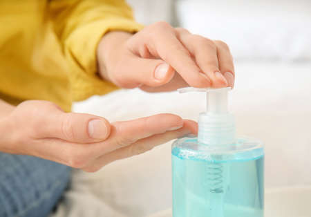 Young woman using sanitizer at home, closeup