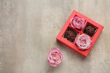 Box with sweets and beautiful pink roses on gray background