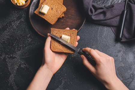 Woman spreading butter onto slice of fresh bread on dark background
