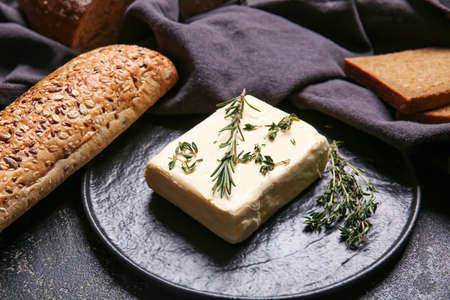 Fresh butter, herbs and bread on dark background