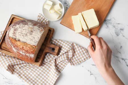 Woman cutting fresh butter on wooden boardの写真素材