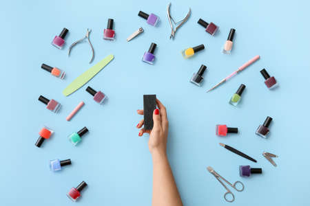 Female hand with nail buffer and tools for manicure on color backgroundの写真素材