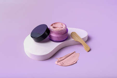 Jar of cosmetic clay with spatula on color background