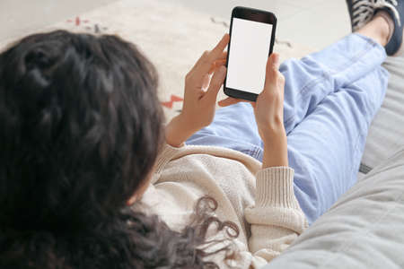 Woman with mobile phone lying on sofa in room