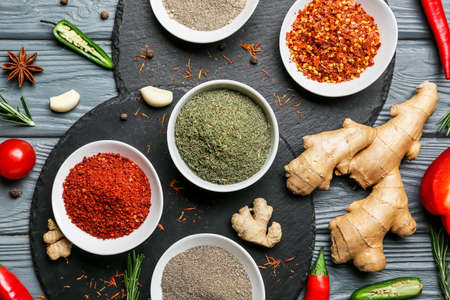 Bowls with different spices and vegetables on dark wooden background