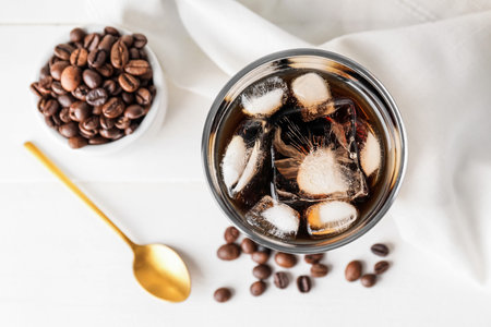 Glass of tasty cold brew and coffee beans on white background