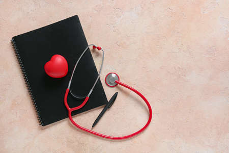 Modern stethoscope, notebook, pen and heart on color backgroundの写真素材