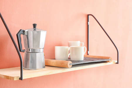 Shelf with coffee maker and cups hanging on color wallの写真素材