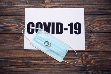 Paper with text COVID-19, rings and mask on wooden background