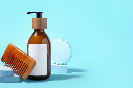 Composition with bottle of natural shampoo and hair comb on color background
