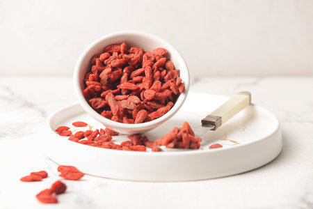 Bowl and spoon with dried goji berries on light background