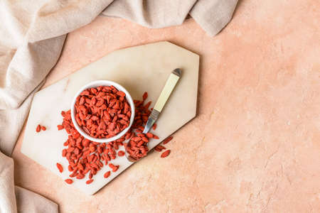 Bowl with dried goji berries on color background