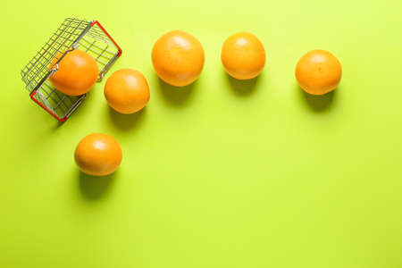 Overturned basket with ripe grapefruits on color background