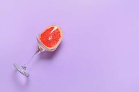 Glass with slice of grapefruit on color background