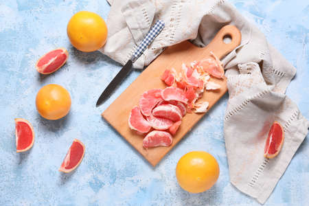 Board with slices of ripe grapefruits on color background