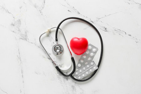 Modern stethoscope with heart and pills on light backgroundの写真素材