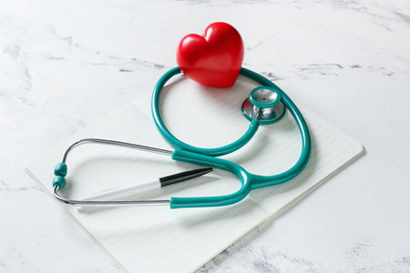 Modern stethoscope with heart and notebook on light backgroundの写真素材